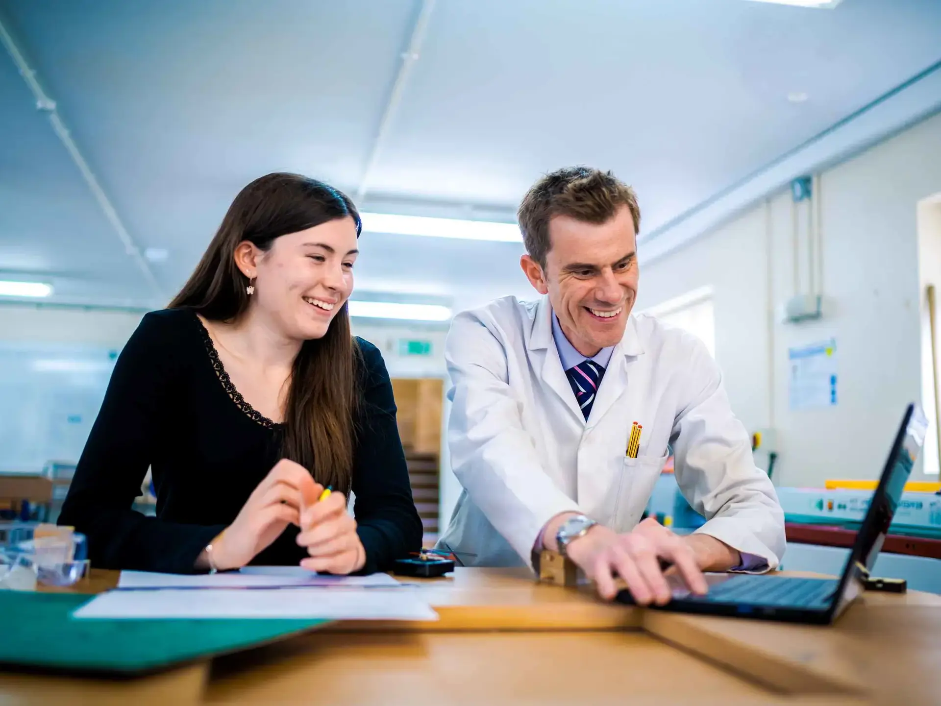 Student and science teacher smiling at laptop