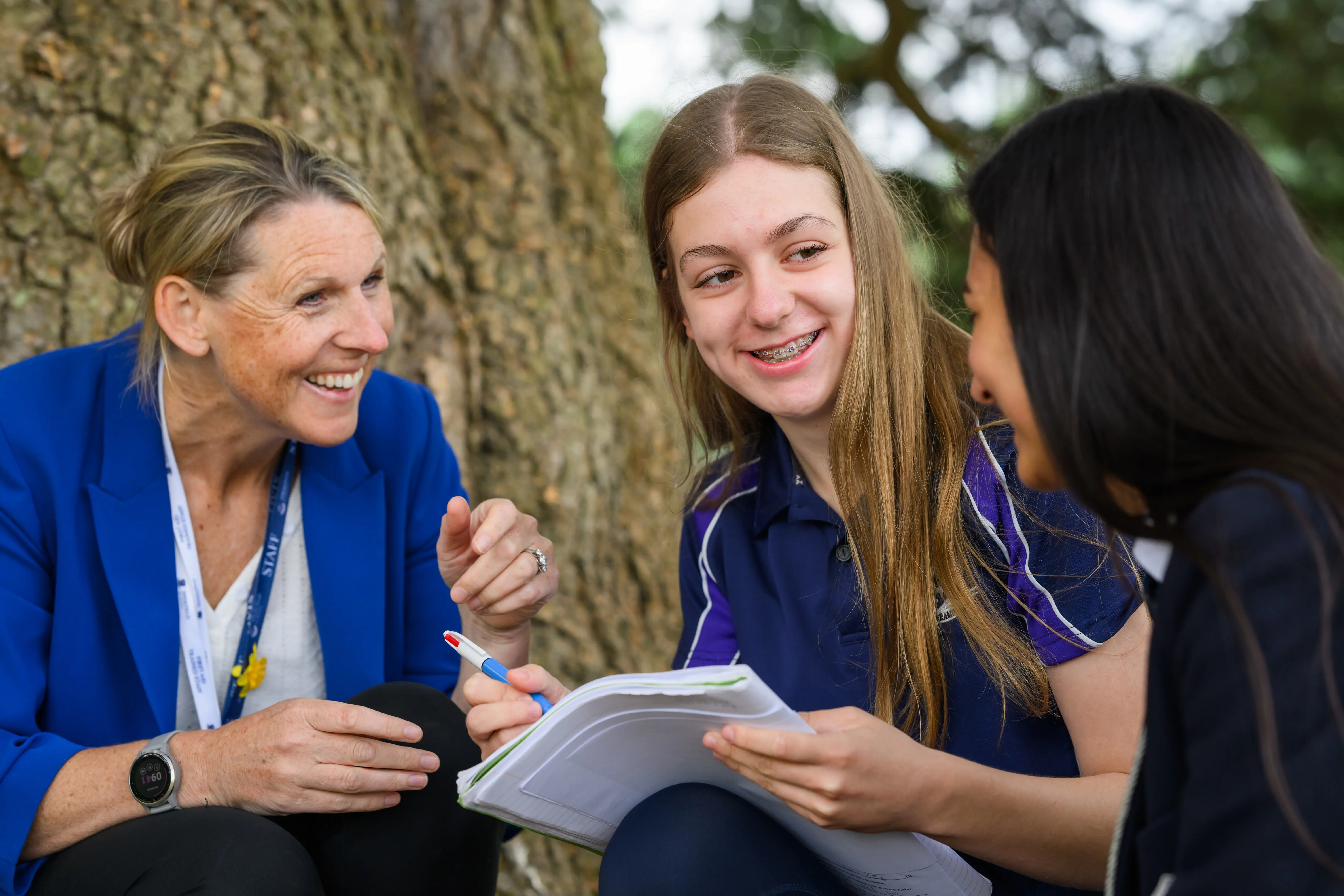 Students and teacher taking notes in front of tree