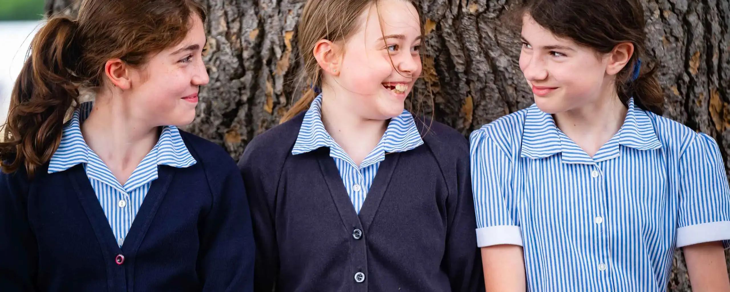 Three students leaning against tree and smiling
