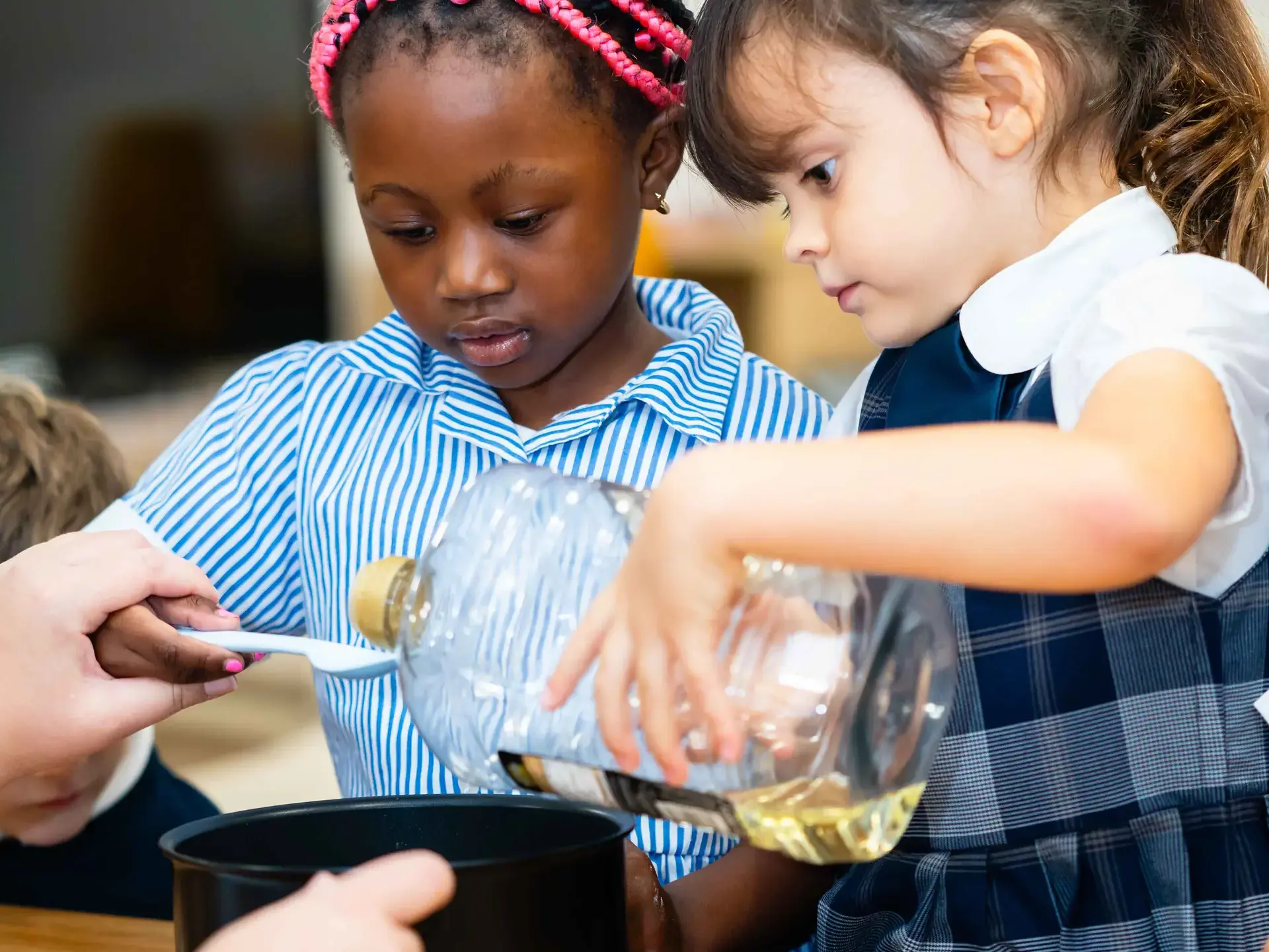 Students pouring oil from large bottle on spoon
